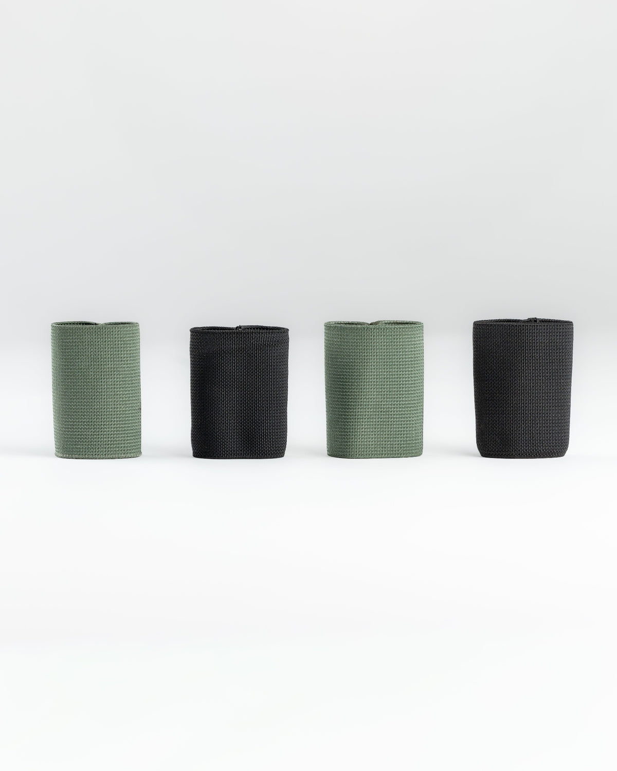 Four SLIM carry accessories arranged in a row on a light gray studio background, alternating between muted sage green and black.