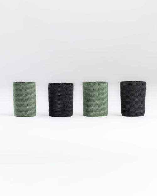 Four SLIM carry accessories arranged in a row on a light gray studio background, alternating between muted sage green and black.