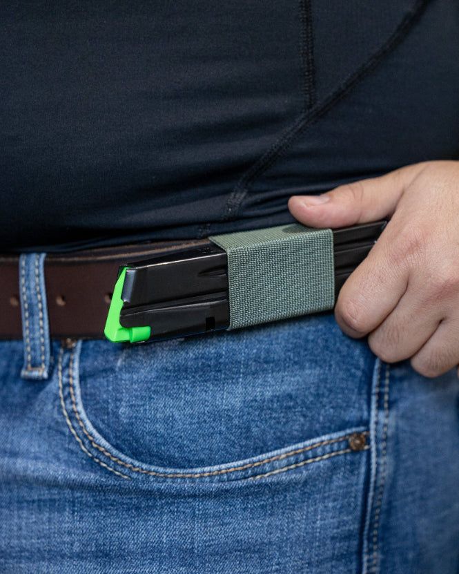 A close-up of a person wearing a green SLIM carry holding a pistol magazine horizontally.