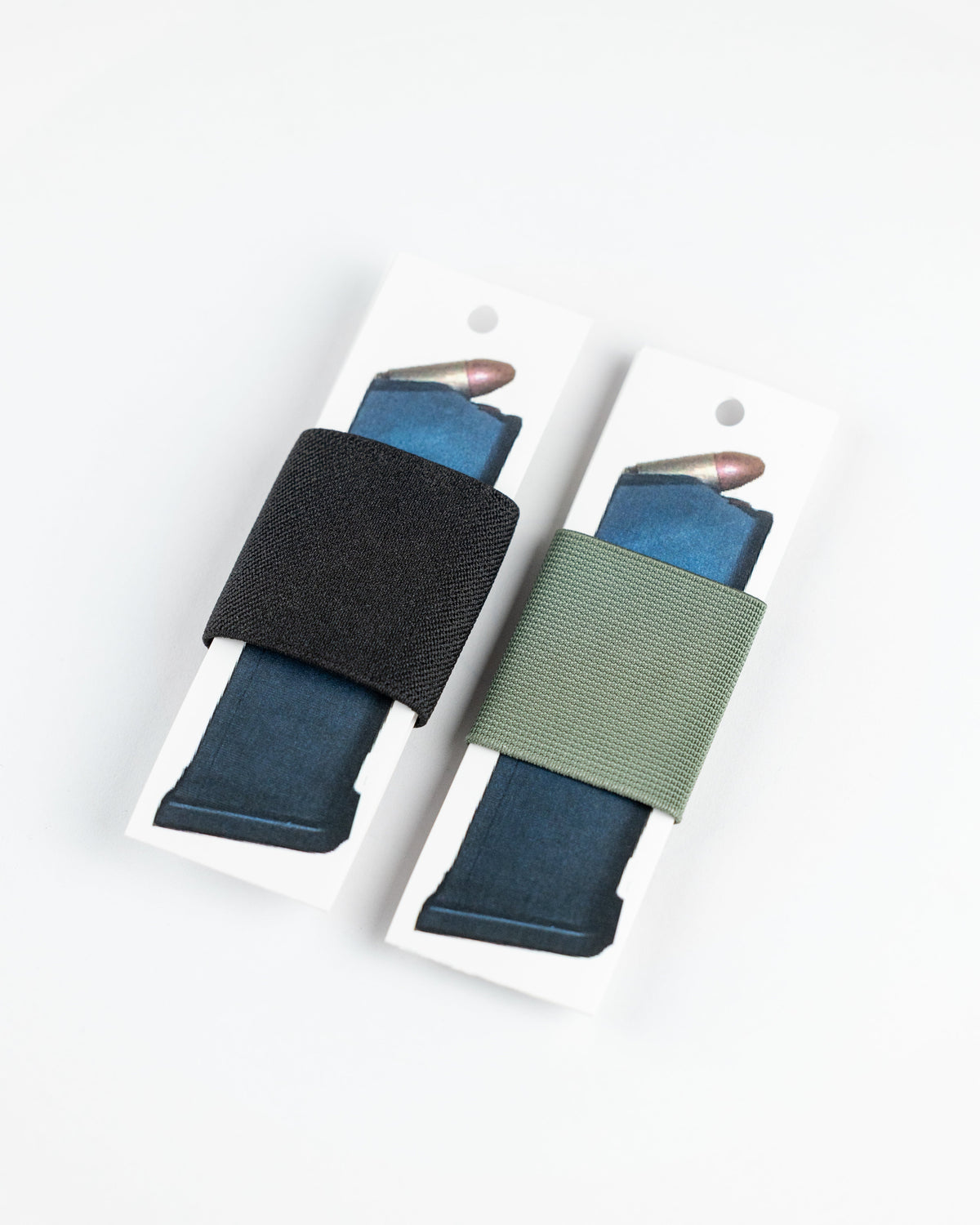 Two SLIM carry accessories. The left loop is black and the right loop is muted green, both holding blue magazines.