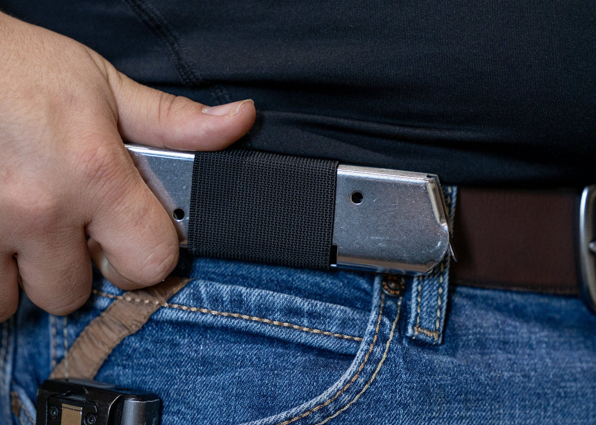 A close-up of a person wearing a black SLIM carry holding a silver magazine.