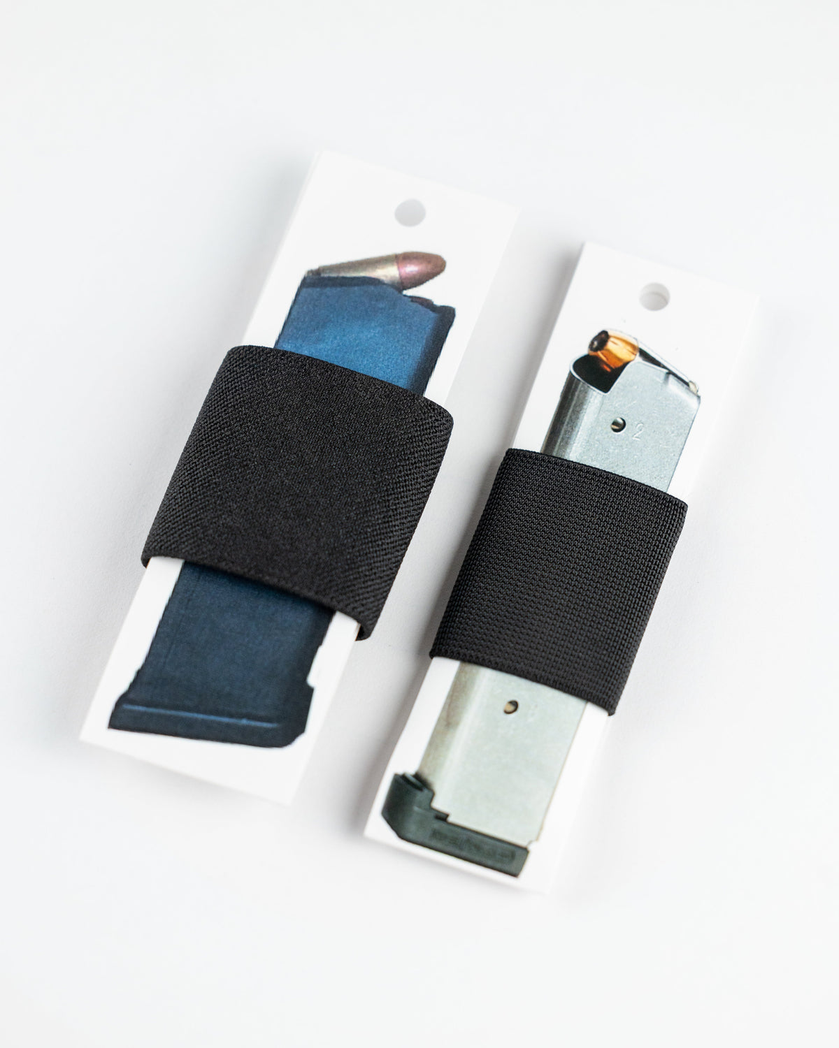 Two black elastic gun magazine straps shown on white backing cards, with one holding a blue magazine and the other holding a silver magazine, on a white background.